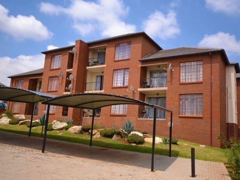 A multi-story apartment building featuring a face brick facade, tiled roof, and covered parking bays with balconies on the upper levels.