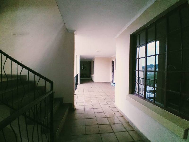 A spacious, tiled apartment hallway featuring a metal staircase railing and large grid-pattern windows, providing a clean and functional transition space.