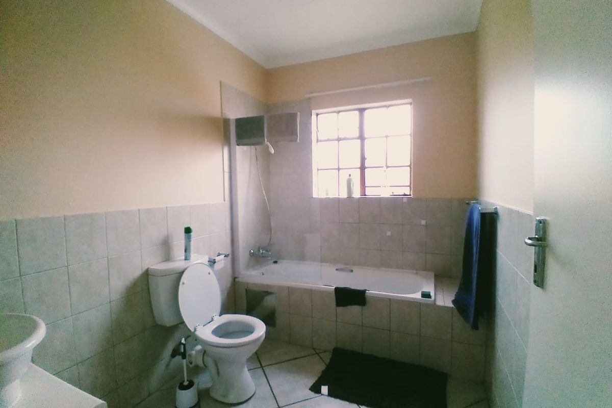 A functional bathroom featuring a bathtub with a glass screen, a toilet, and a washbasin, finished with neutral wall and floor tiles.
