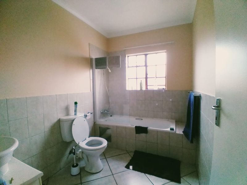 A functional bathroom featuring a bathtub with a glass screen, a toilet, and a washbasin, finished with neutral wall and floor tiles.