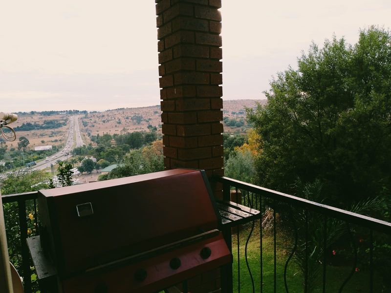 An elevated balcony featuring a brick pillar and metal railing, offering expansive views of the surrounding landscape and nearby road.