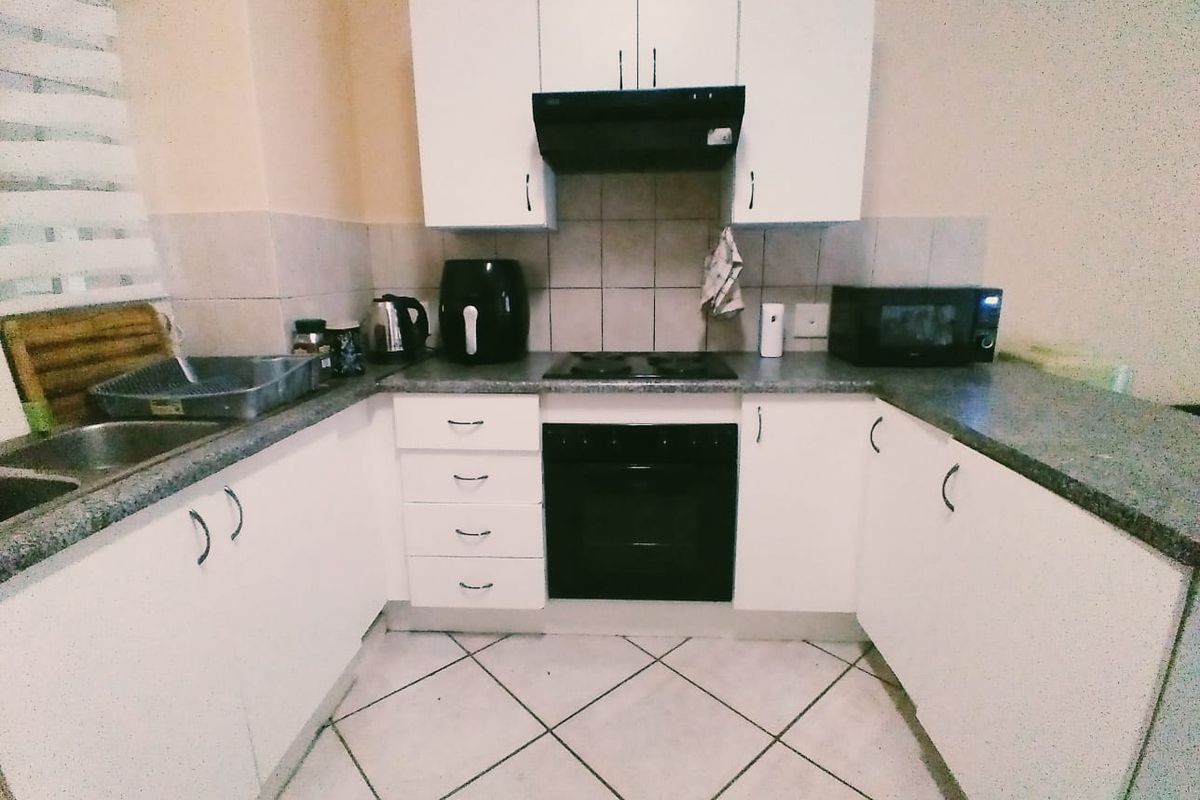 A functional U-shaped kitchen featuring white cabinetry, dark laminate countertops, a built-in oven with hob, and tiled flooring.