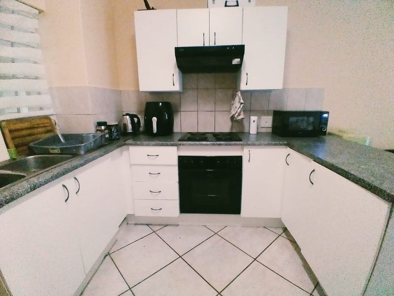 A functional U-shaped kitchen featuring white cabinetry, dark laminate countertops, a built-in oven with hob, and tiled flooring.