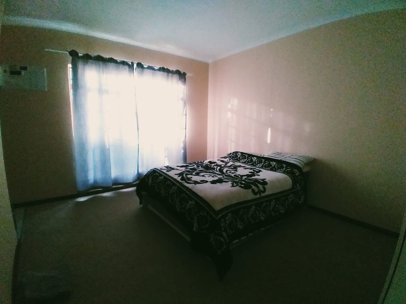 A simple bedroom featuring carpeted flooring and a window with curtains, providing a functional and neutral space.