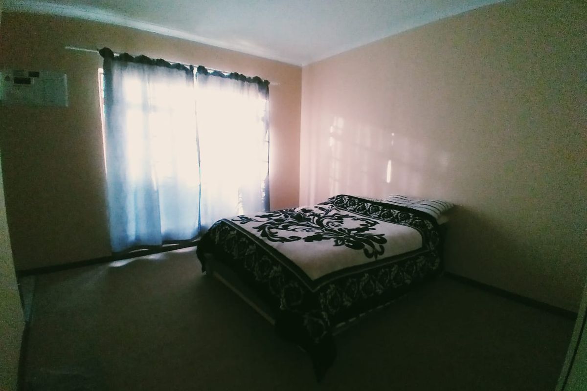 A simple bedroom featuring carpeted flooring and a window with curtains, providing a functional and neutral space.
