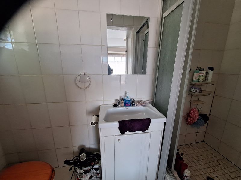 A compact bathroom featuring a vanity cabinet with basin, wall-mounted mirror, and a separate shower enclosure with tiled finishes.
