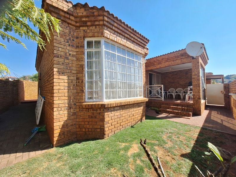 Rear view of a face brick townhouse featuring a bay window, a covered patio area, and a small private garden space.