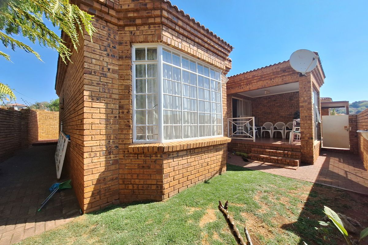 Rear view of a face brick townhouse featuring a bay window, a covered patio area, and a small private garden space.