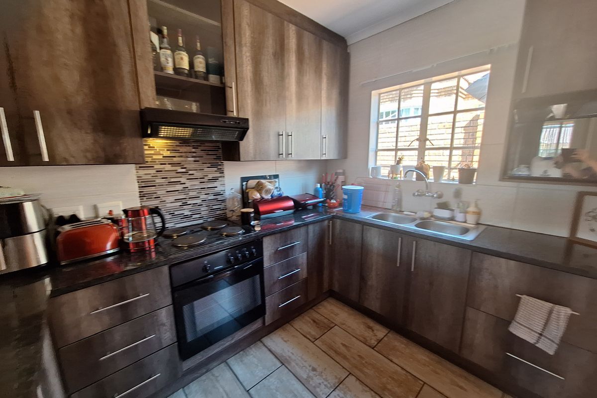 A functional kitchen featuring dark wood-look cabinetry, granite-style countertops, a mosaic backsplash, and integrated appliances including an oven and extractor fan.