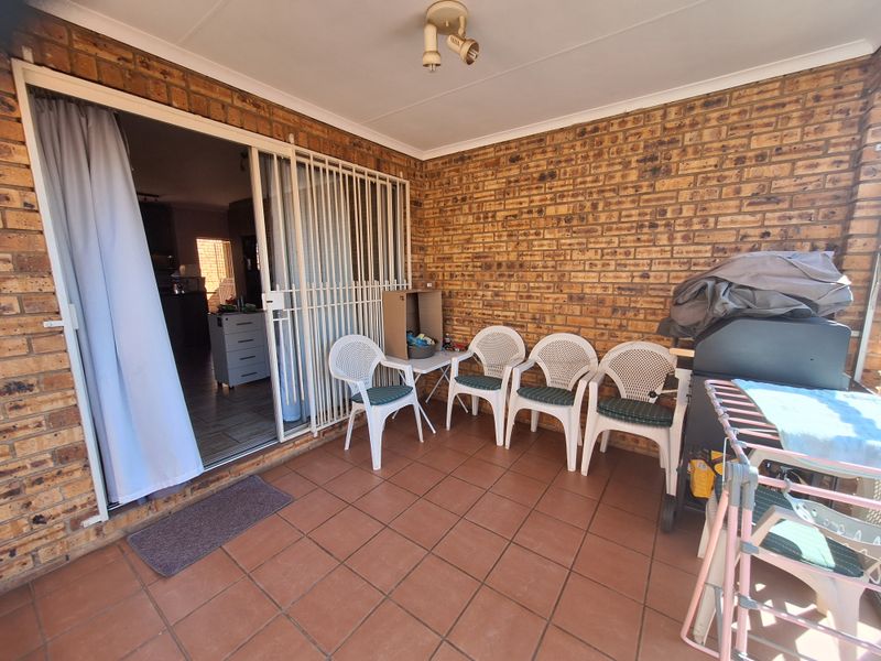 A covered patio area featuring exposed brick walls, tiled flooring, and a security gate providing access to the interior living space.