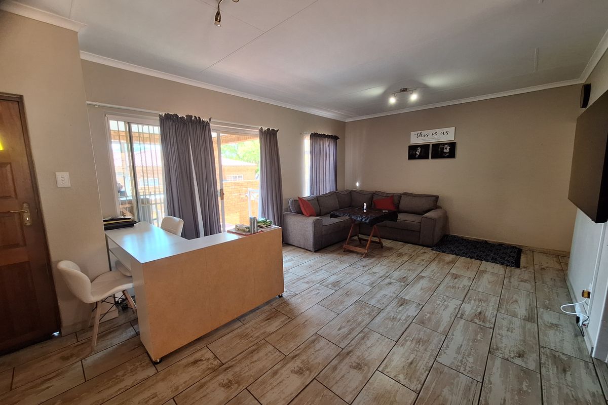 Spacious living room featuring wood-look tiled flooring, sliding glass doors leading to the patio, and neutral wall finishes.