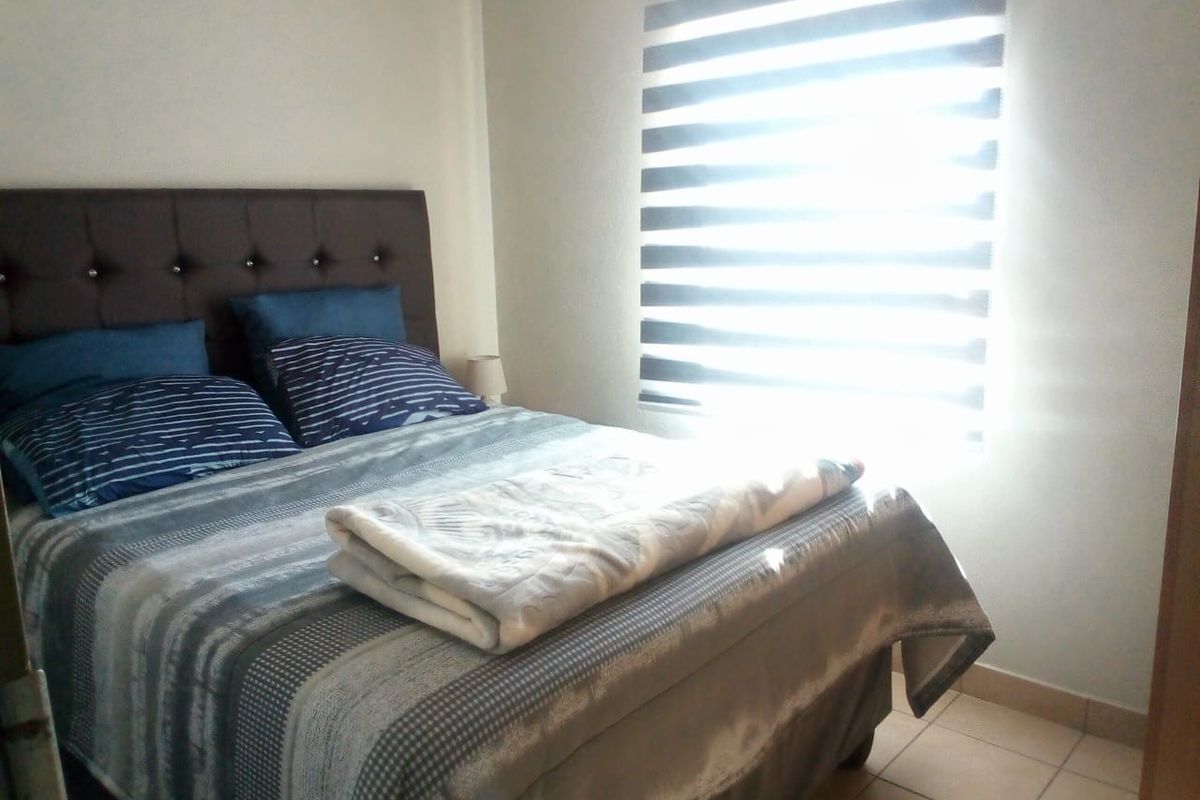A functional bedroom featuring tiled flooring and modern zebra blinds, providing a simple and comfortable sleeping space.