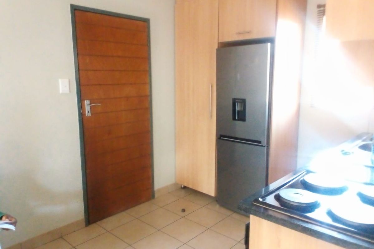 A functional kitchen area featuring built-in wooden cabinetry, a hob, and tiled flooring, with a solid wood door leading to the adjacent space.