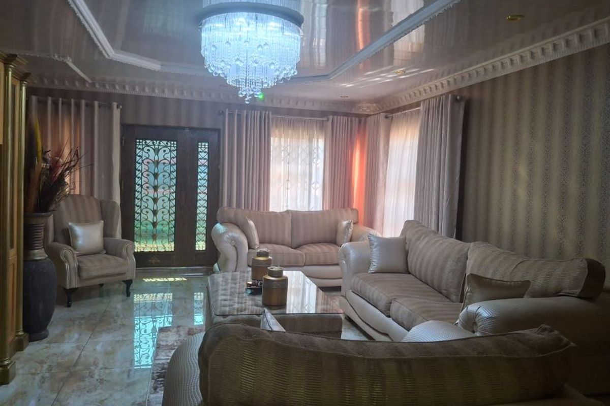 A formal living room featuring glossy tiled floors, decorative ceiling molding, a recessed tray ceiling, and an ornate metal security entrance door.