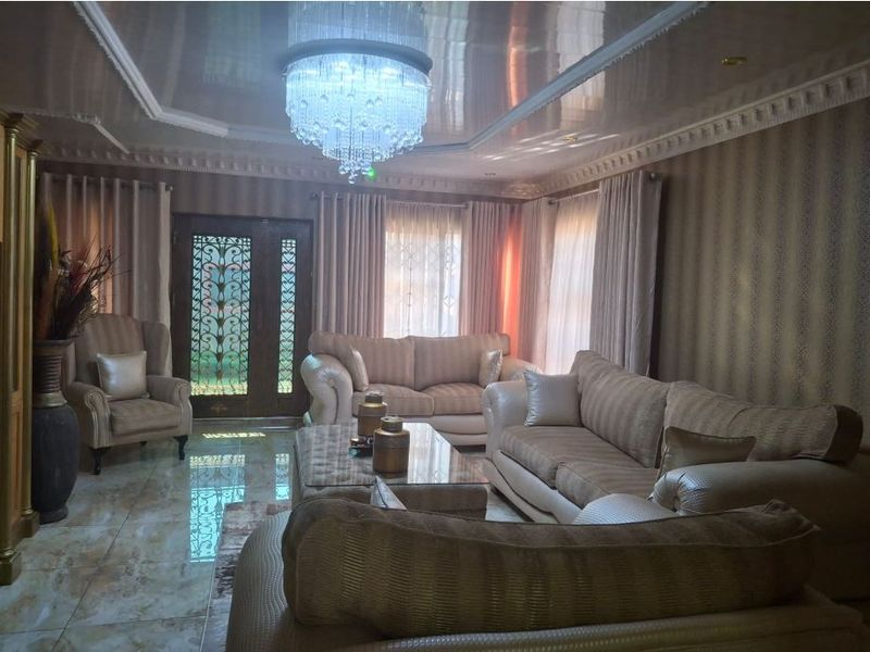 A formal living room featuring glossy tiled floors, decorative ceiling molding, a recessed tray ceiling, and an ornate metal security entrance door.