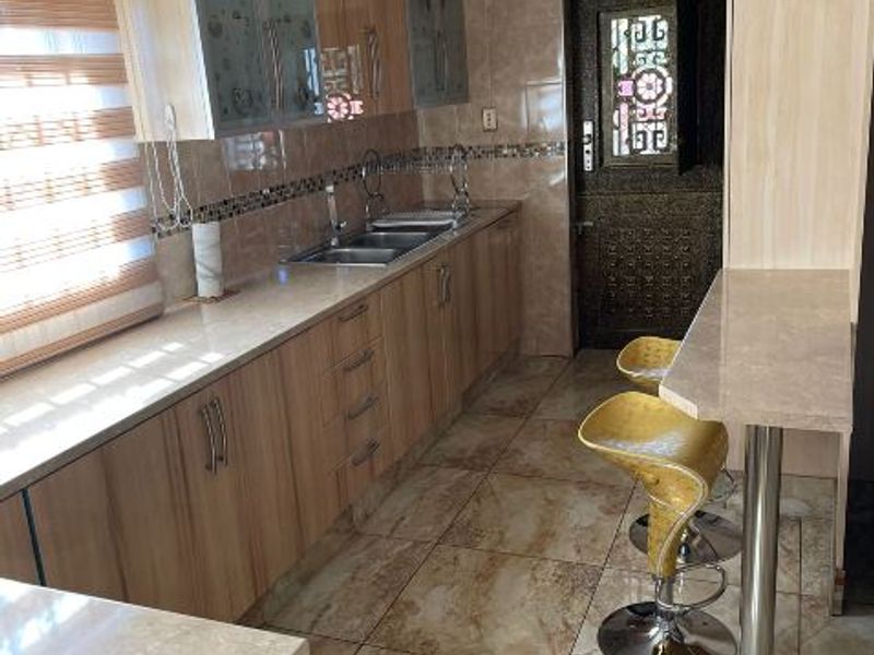 A functional kitchen featuring wood-look cabinetry, stone-style countertops, a breakfast bar, and tiled flooring with a neutral backsplash.