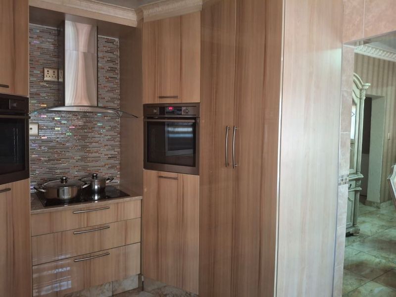 A modern kitchen featuring wood-finish cabinetry, a mosaic tile backsplash, built-in oven, and a sleek extractor fan over the hob.