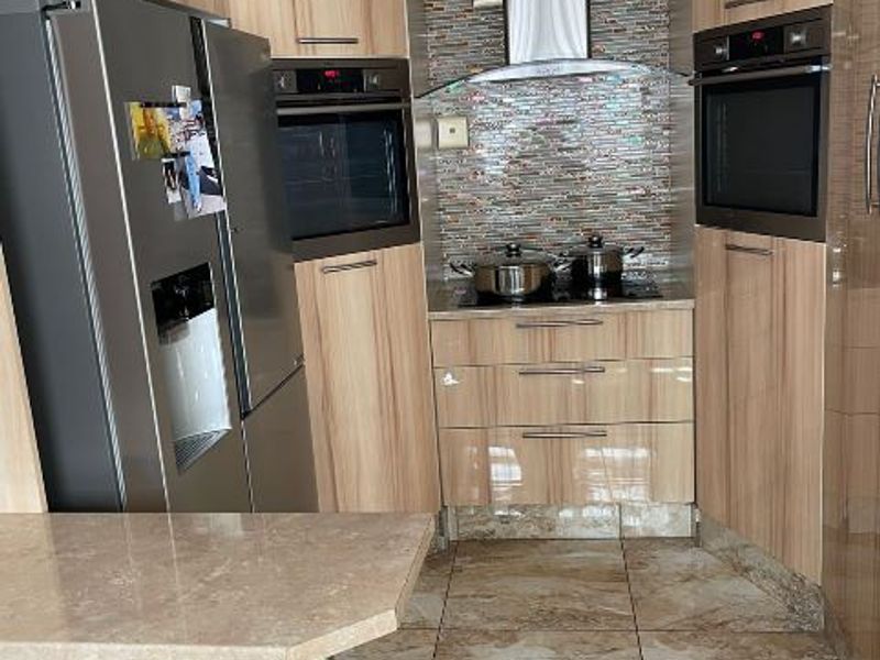 A modern kitchen featuring wood-grain cabinetry, built-in ovens, a stainless steel extractor fan, mosaic tile backsplash, and polished tiled flooring.