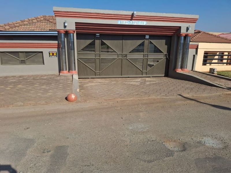 Front elevation of the property featuring a paved driveway, secure automated sliding gate, and decorative architectural pillars.