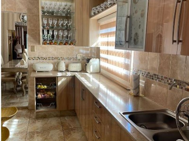 A well-maintained kitchen featuring wood-finish cabinetry, tiled flooring, a double stainless steel sink, and a decorative glass display cabinet.