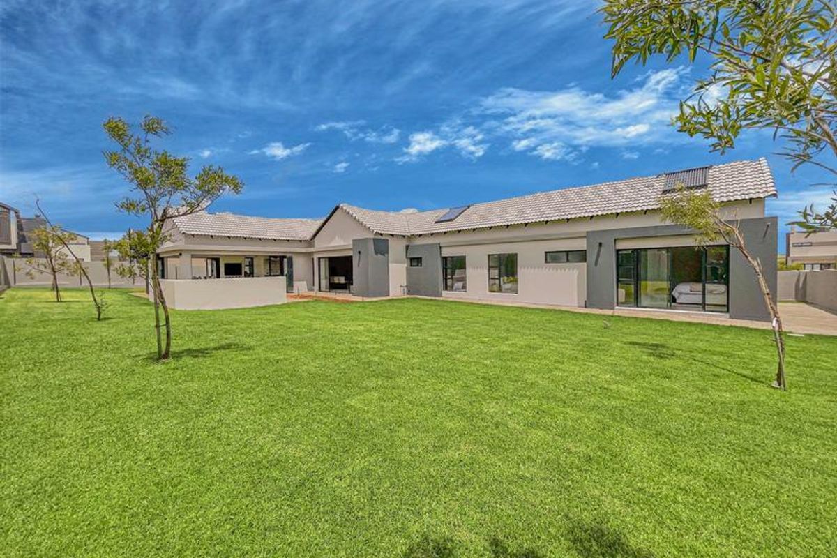 Spacious rear garden featuring a well-maintained lawn, modern exterior facade with large sliding glass doors, and a covered patio area.