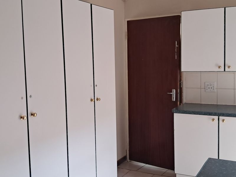 A functional kitchen area featuring built-in white cabinetry, laminate countertops, tiled splashback, and a stainless steel sink.