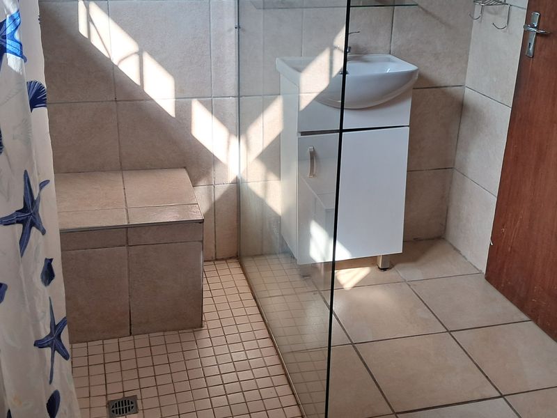 A functional bathroom featuring a tiled walk-in shower with a built-in bench, glass partition, and a modern vanity basin.