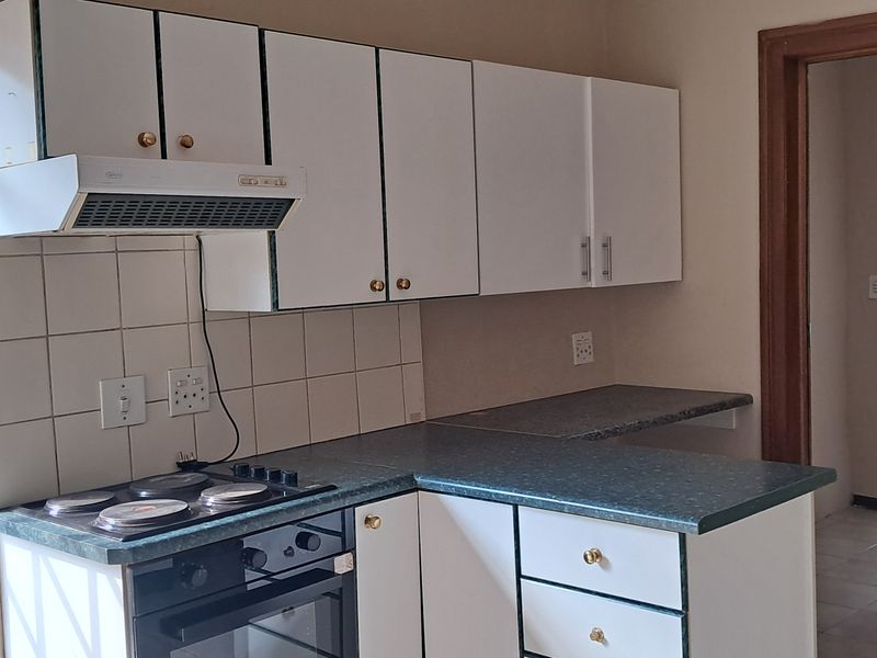 A functional kitchen featuring white cabinetry, a built-in oven and hob, extractor fan, and laminate countertops with a tiled splashback.