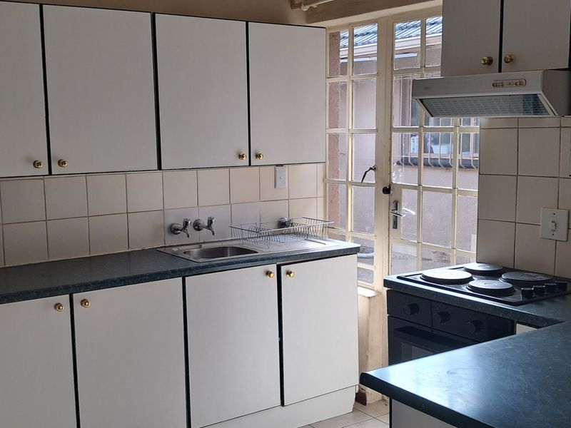 A functional kitchen featuring white cabinetry, dark laminate countertops, a built-in electric hob and oven, and tiled splashbacks with direct access to the exterior.