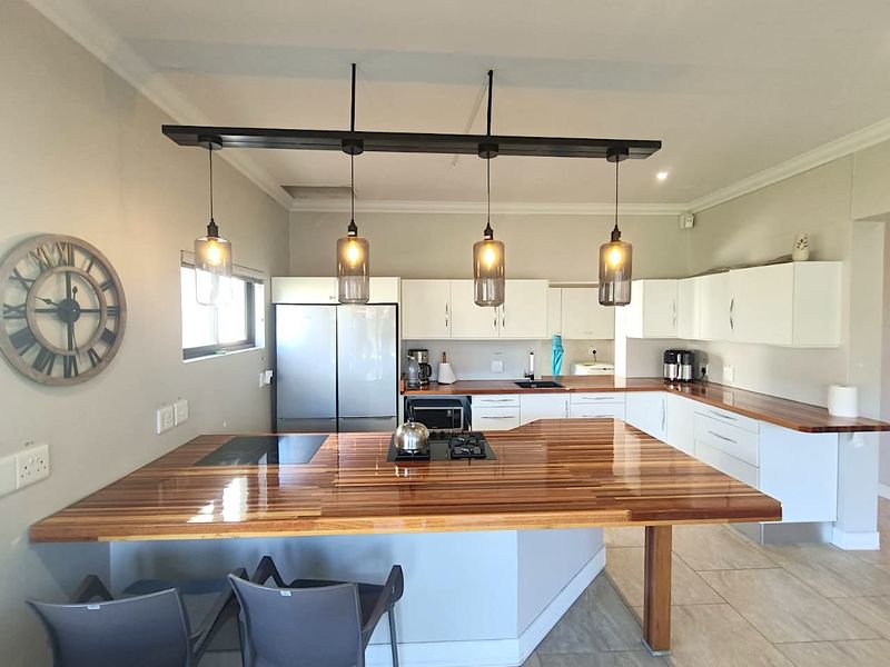 Modern kitchen featuring a large wooden breakfast bar, white cabinetry, built-in hob, and stylish pendant lighting.