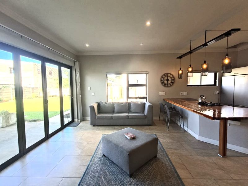 Spacious open-plan living and kitchen area featuring tiled floors, modern pendant lighting, a breakfast bar, and large bi-fold doors opening to the garden.