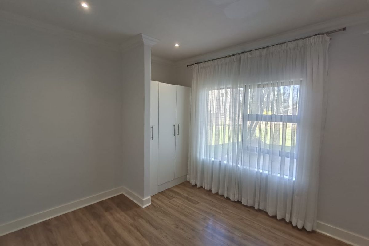 A bright, vacant bedroom featuring modern laminate flooring, built-in cupboards, and recessed downlighting, offering a clean and neutral space ready for personalization.