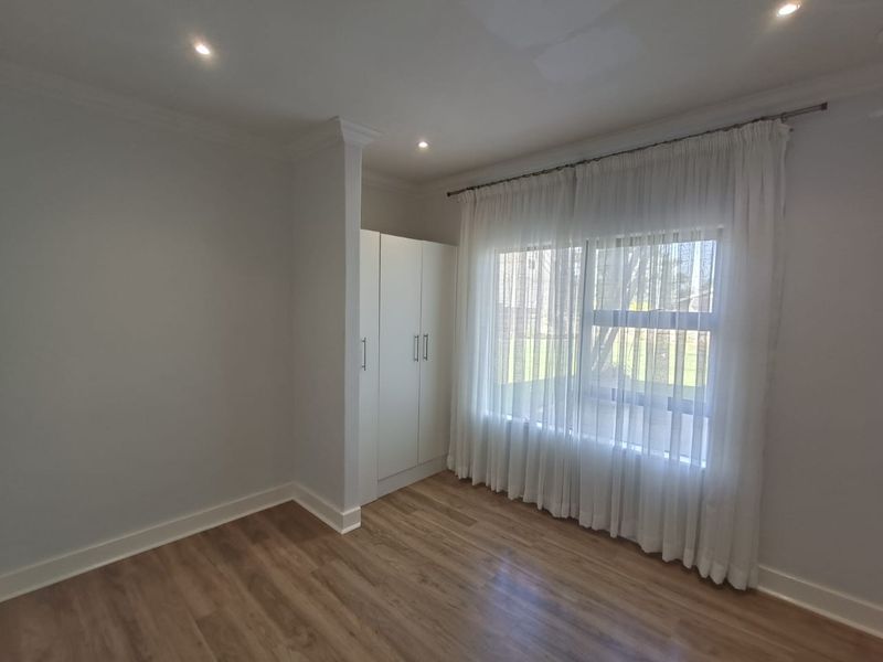 A bright, vacant bedroom featuring modern laminate flooring, built-in cupboards, and recessed downlighting, offering a clean and neutral space ready for personalization.
