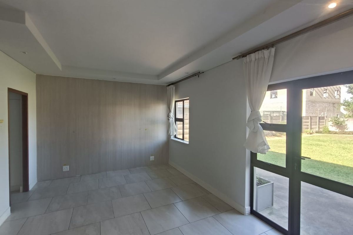 A bright, empty living area featuring large format floor tiles, a modern accent wall, and direct access to the garden through glass doors.