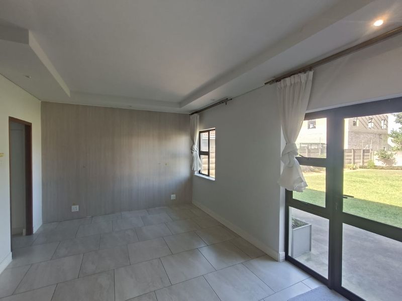 A bright, empty living area featuring large format floor tiles, a modern accent wall, and direct access to the garden through glass doors.