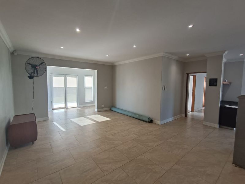 Spacious open-plan living area featuring neutral tiled flooring, recessed downlights, and sliding glass doors providing access to the exterior.