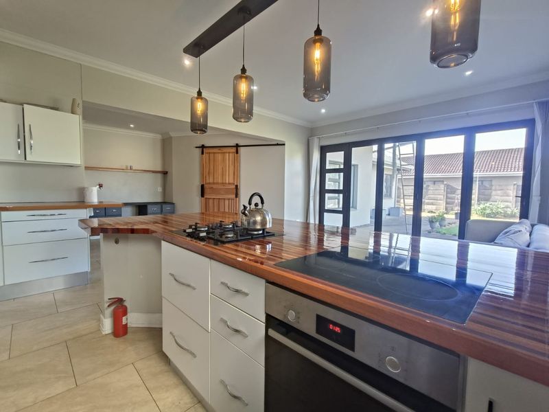Modern kitchen featuring a large wooden island with integrated gas and induction hobs, built-in oven, pendant lighting, and direct access to the rear patio.