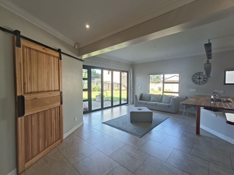 Spacious open-plan living area featuring tiled floors, a sliding barn door, and large aluminium stacker doors providing seamless access to the rear garden.