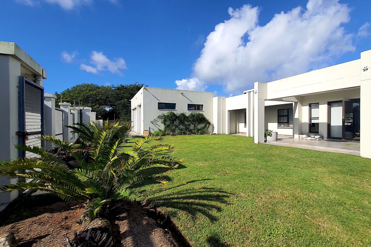 A spacious rear garden featuring a well-maintained lawn, a covered patio area, and modern architectural lines with sliding glass doors.