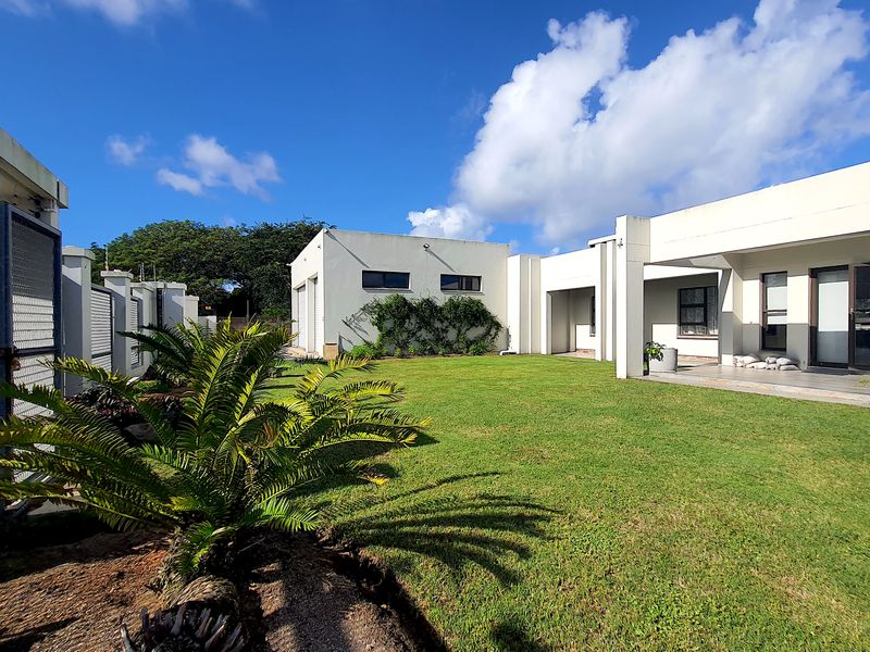 A spacious rear garden featuring a well-maintained lawn, a covered patio area, and modern architectural lines with sliding glass doors.