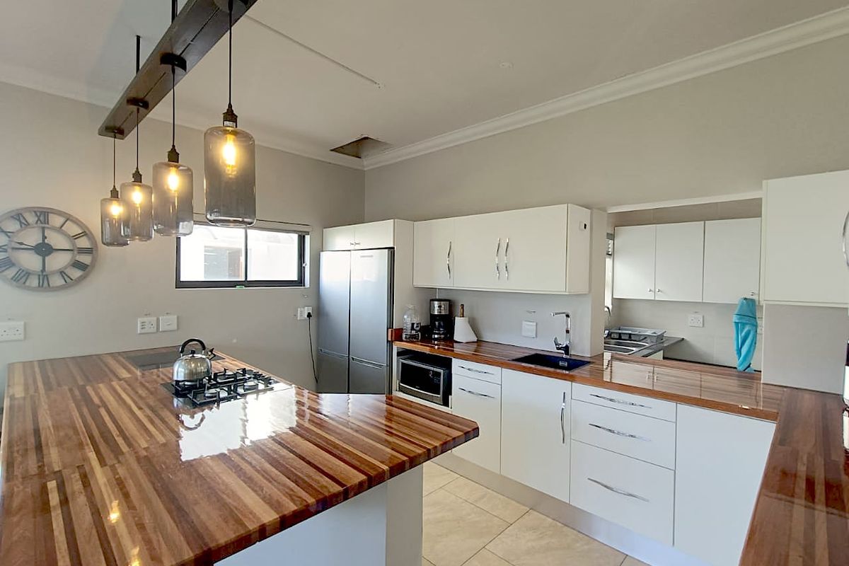 Modern kitchen featuring white cabinetry, warm wooden countertops, a gas hob, and a convenient adjoining scullery area with ample storage.