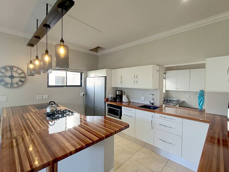 Modern kitchen featuring white cabinetry, warm wooden countertops, a gas hob, and a convenient adjoining scullery area with ample storage.