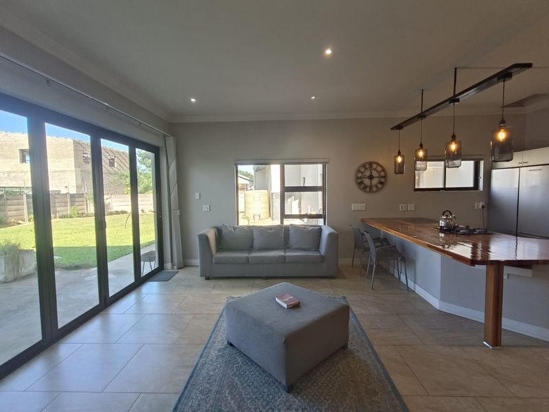 Spacious open-plan living area featuring tiled floors, modern pendant lighting, a breakfast bar, and large sliding doors providing seamless access to the garden.