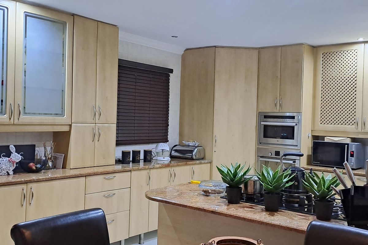 A functional kitchen featuring light wood cabinetry, granite countertops, a central island with a built-in hob, and integrated oven and microwave units.