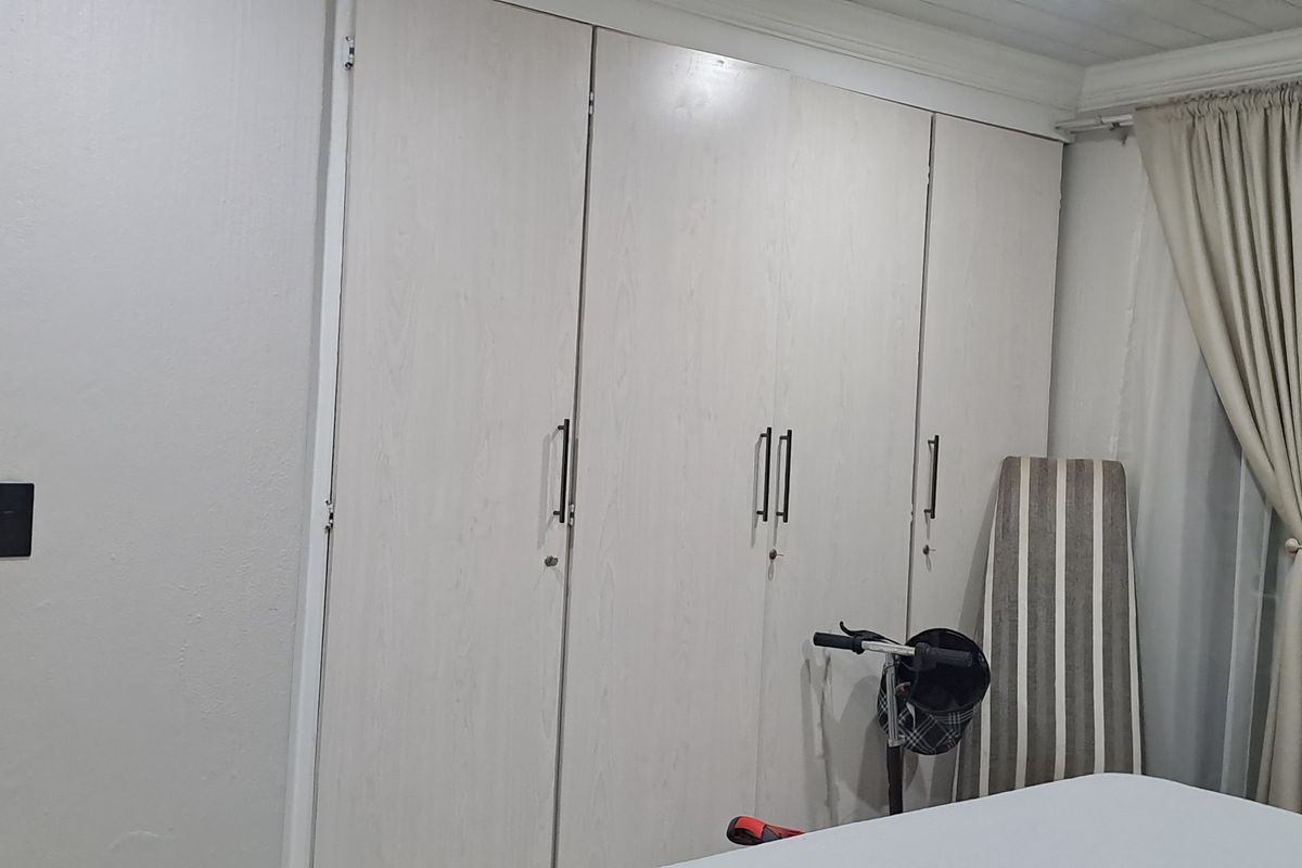 A bedroom featuring built-in floor-to-ceiling wardrobes with light wood-grain finish and crown molding.