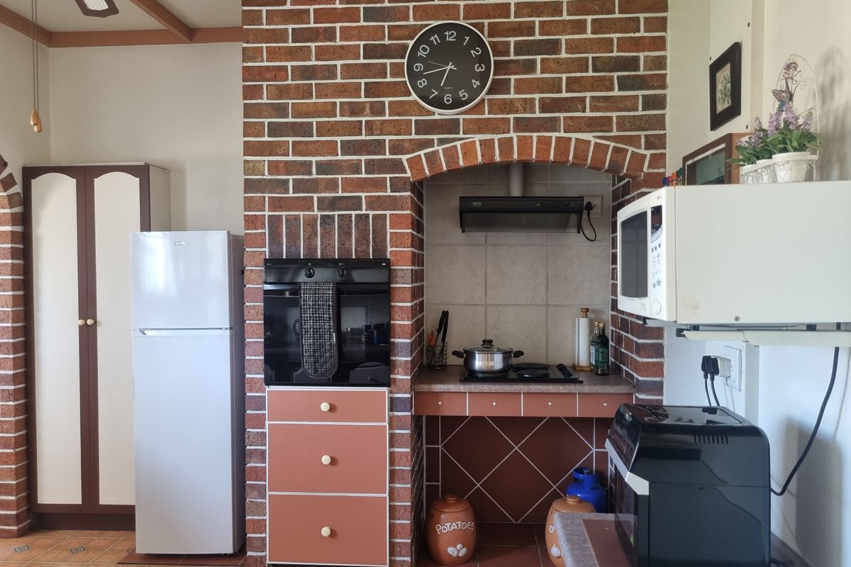 Kitchen featuring a rustic brick feature wall with built-in oven, hob, and extractor fan, complemented by tiled flooring and functional cabinetry.