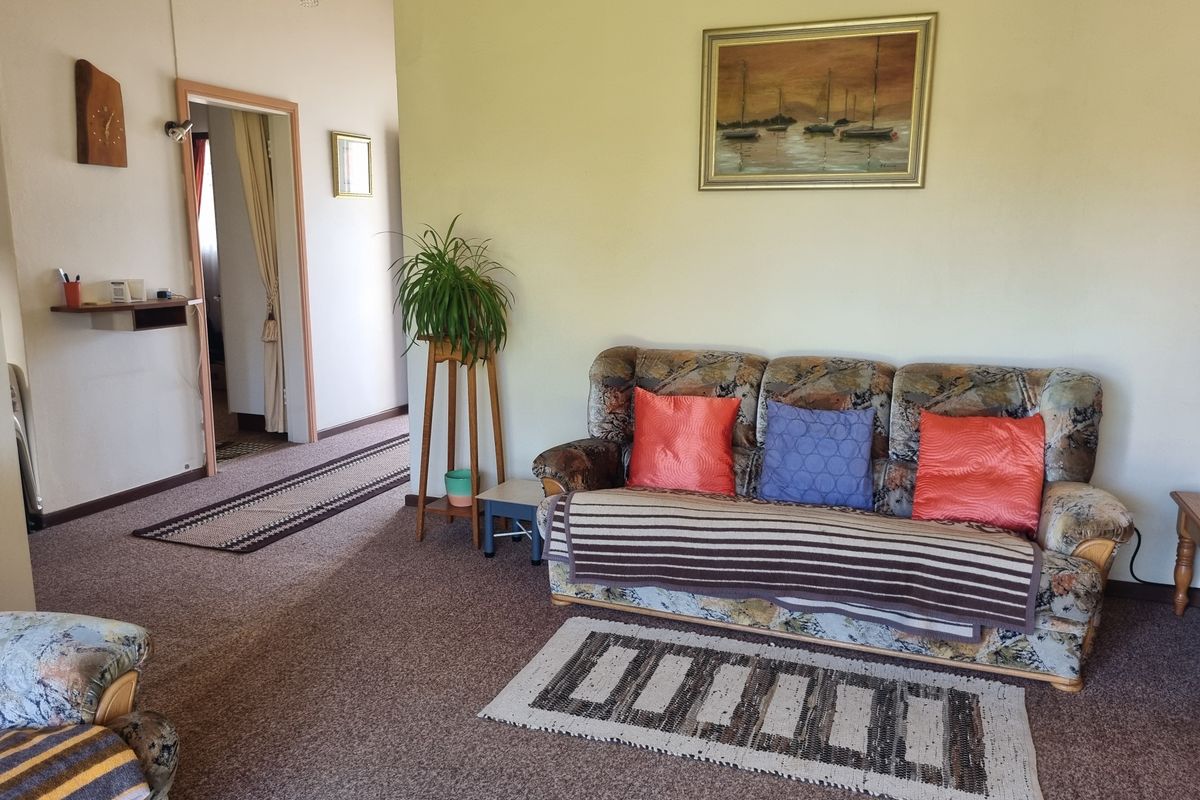A living room area featuring carpeted flooring and neutral wall finishes, providing a functional space with access to an adjoining hallway.