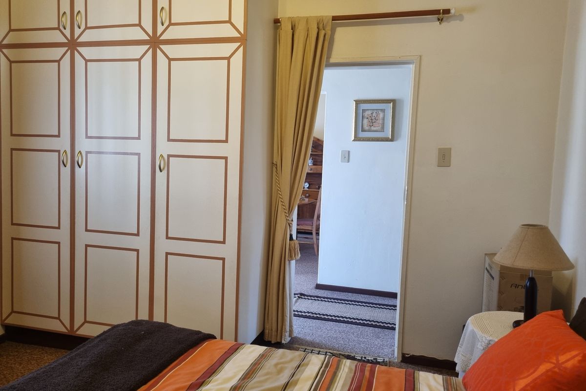 A bedroom featuring built-in wardrobes and carpeted flooring, with a doorway leading to an adjacent room.