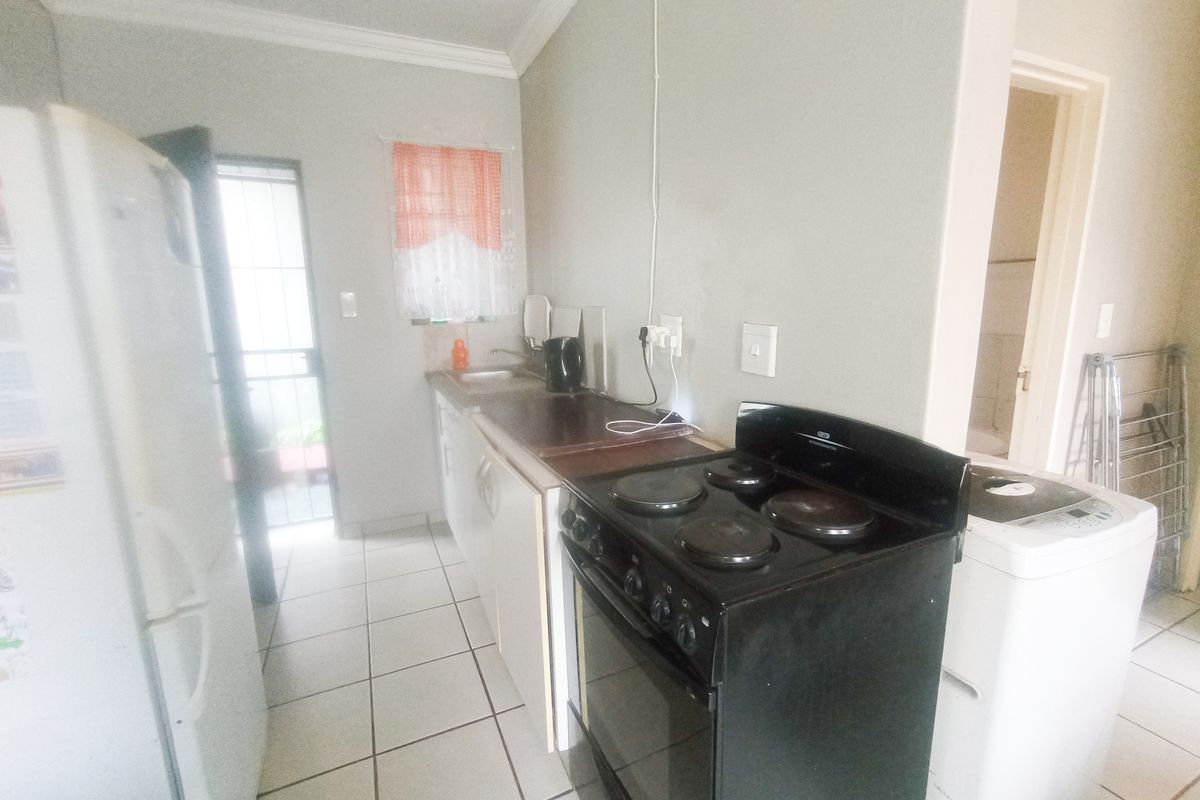 A compact kitchen featuring tiled flooring, built-in cabinetry, and a freestanding stove, with direct access to an exterior security gate.