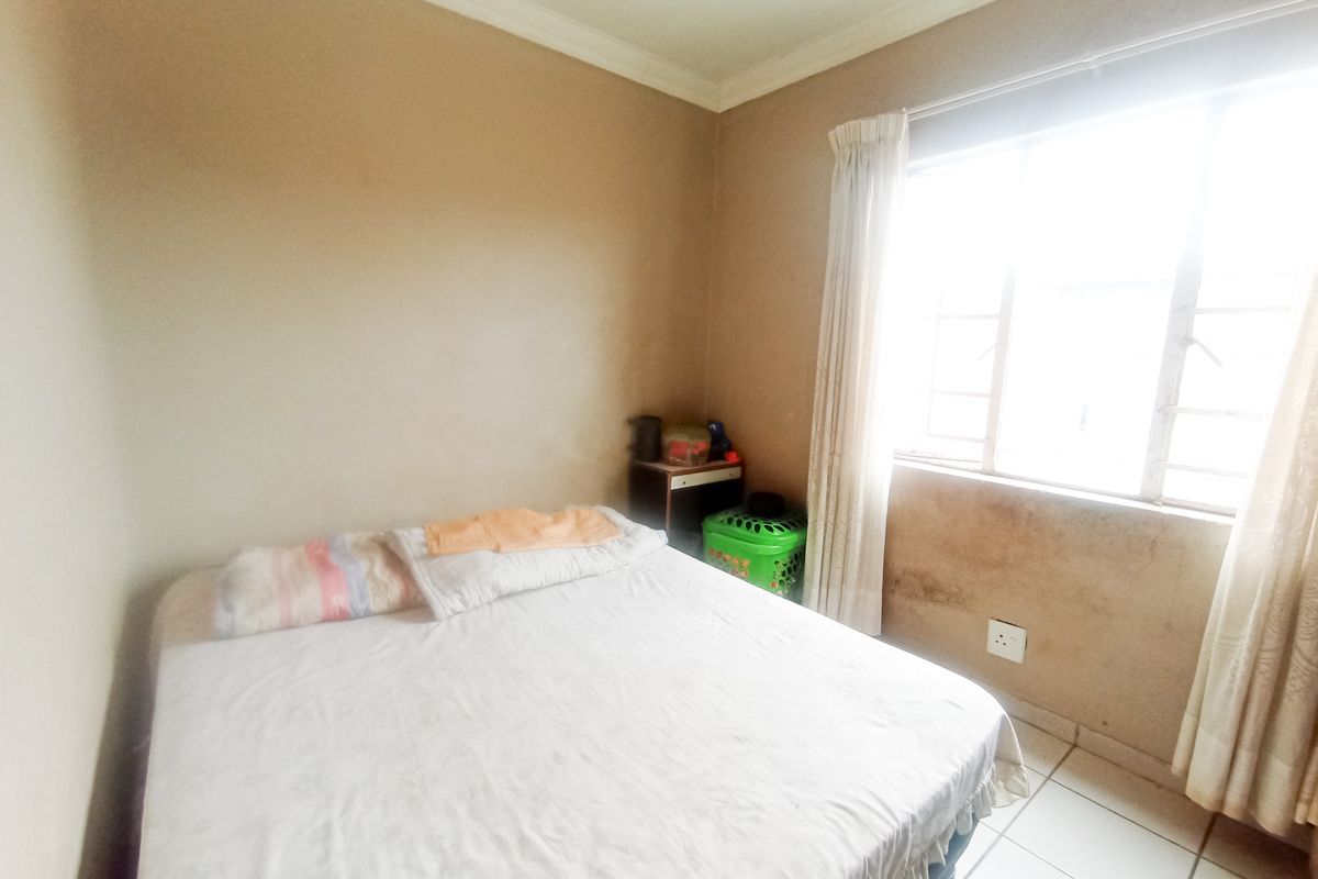 A bedroom featuring tiled flooring and a window, currently showing signs of wall staining and wear that would benefit from cosmetic updates.